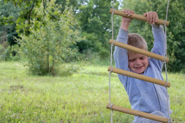 Boy climbing on rope ladder in garden — Stock Photo, Image