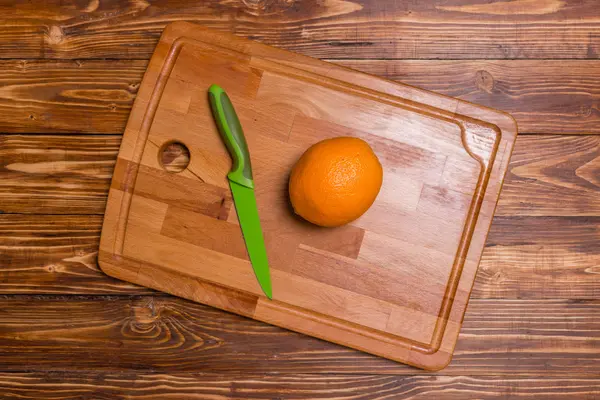 Čerstvý pomeranč a zelený nůž na dřevěné desce — Stock fotografie
