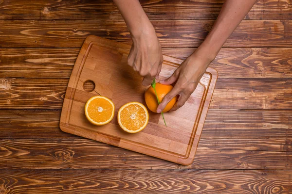 Woman is cutting orange on wooden board in the kitchen, top view — Stock Photo, Image