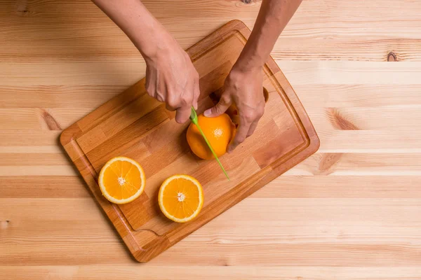 Woman cuts the orange slices on a wooden board, top view — Stock Photo, Image