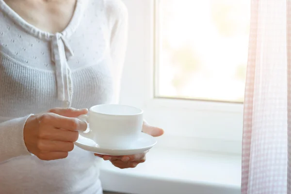 Young woman's hands is holding hot cup of coffee or tea in morning sunlight — Stock Photo, Image