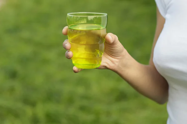 Woman is holding water glass in garden on green grass background — Stock Photo, Image