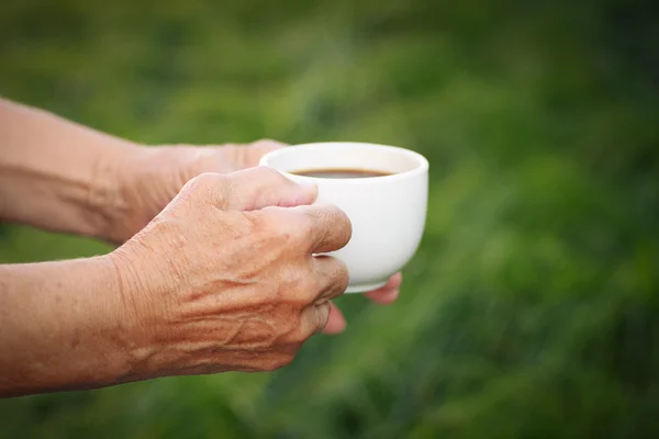 Starší žena držící šálek horké kávy ve své zahradě — Stock fotografie
