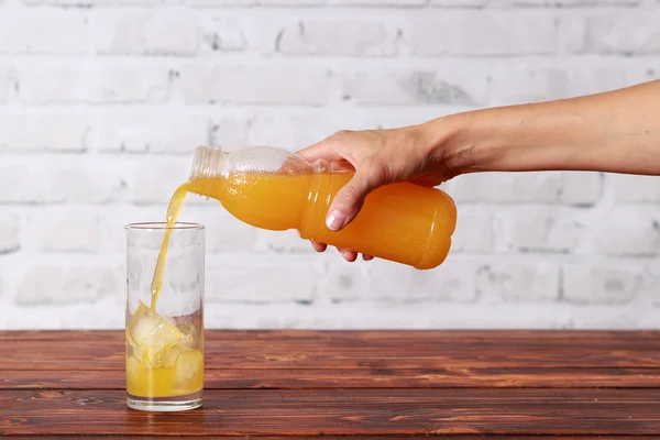 Girl's hand with bottle of orange juice pouring it in glass with ice cubes — Stock Photo, Image
