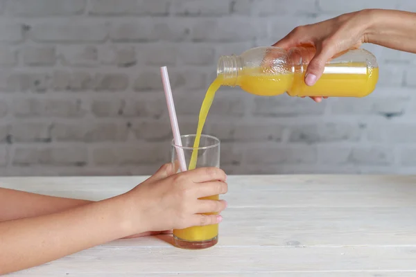 Mother pouring her daughter some orange juice in glass from bottle — Stock Photo, Image