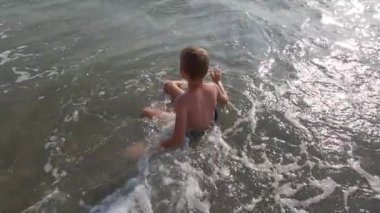 Küçük çocuk sahilde dalgalar içinde eğleniyor.