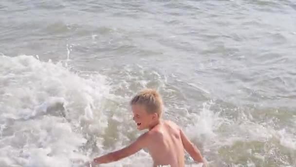 Мальчик веселится в волнах на пляже — стоковое видео