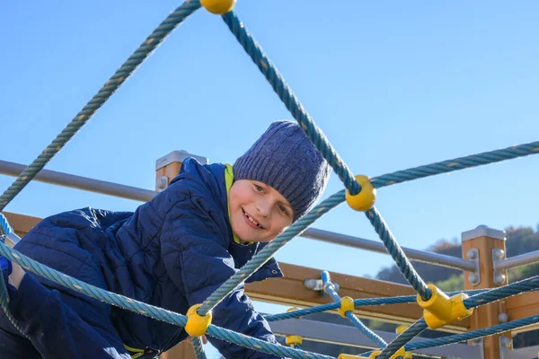 Little boy climbing on rope in playground at sunny autumn day — Stock Photo, Image