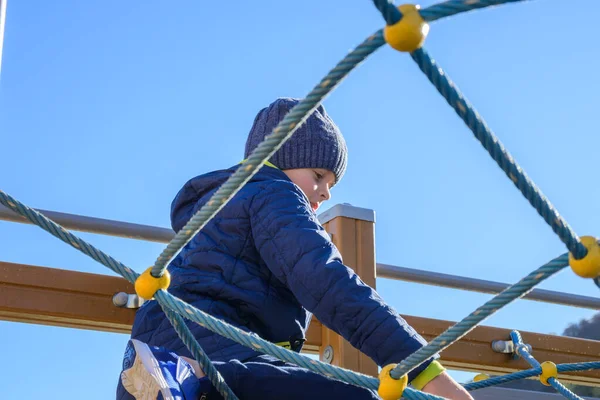 Little boy climbing on rope in playground at sunny autumn day — Stock Photo, Image