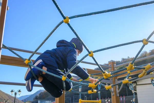 Little boy climbing on rope in playground at sunny autumn day — Stock Photo, Image