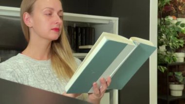 Evde kitap okuyan genç bir kadın koltukta oturuyor.