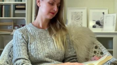 Evde kitap okuyan genç bir kadın koltukta oturuyor.