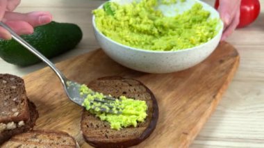 Kadın eli tostun üzerine avokado koyar.