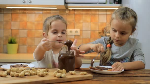 Маленькие девочки готовят сэндвич с арахисовым маслом и едят его — стоковое видео