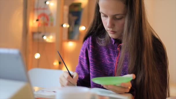 Dibujo de niña con pincel en papel y mirando lección en la tableta — Vídeo de stock