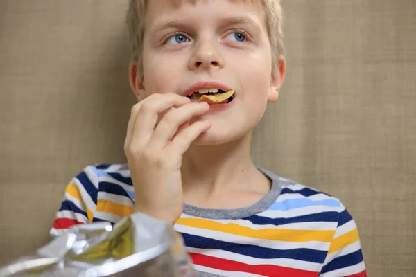 Kleiner Junge sitzt auf Sofa und isst Chips aus Päckchen — Stockfoto