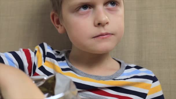 Little boy sitting on sofa, eating chips from packet — Stock Video