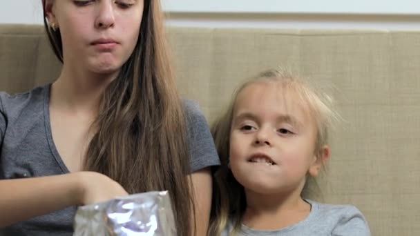 Dos hermanas comiendo papas fritas y mirando algo en la televisión — Vídeo de stock