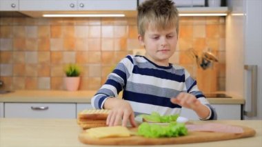 Küçük çocuk mutfakta salata ve peynirli sandviç yiyor.