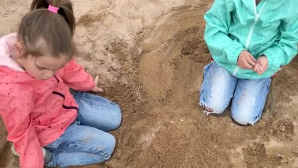 Två små systrar leker med sand och snäckskal på stranden — Stockvideo