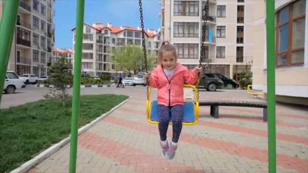 Glückliche kleine Mädchen schaukeln auf städtischem Spielplatz — Stockvideo
