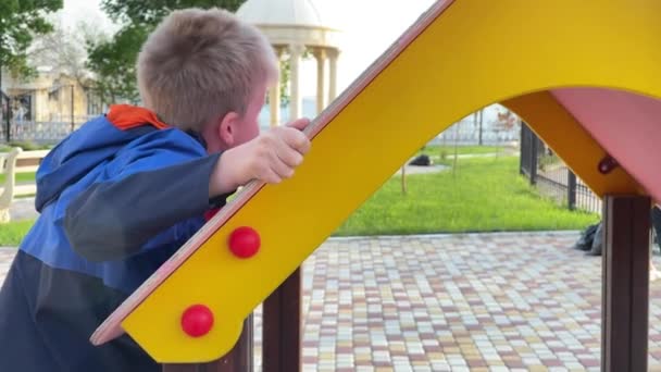 Усміхнений хлопчик тренується на дитячому майданчику — стокове відео