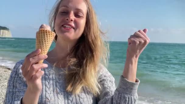 Glücklich lächelnde Frau, die am Meer spaziert und Eis isst — Stockvideo