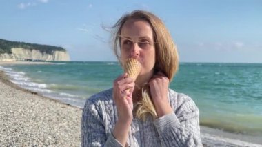 Deniz kenarında dinlenen ve dondurma yiyen bir kadın. 
