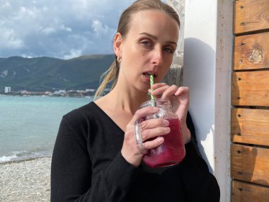 Mutlu kadın deniz kenarında meyve suyu içiyor, ağır çekimde.