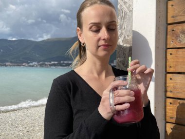 Mutlu kadın deniz kenarında meyve suyu içiyor, ağır çekimde.