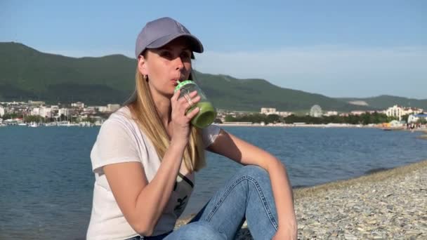 Donna che beve frullato verde disintossicante sulla spiaggia — Video Stock