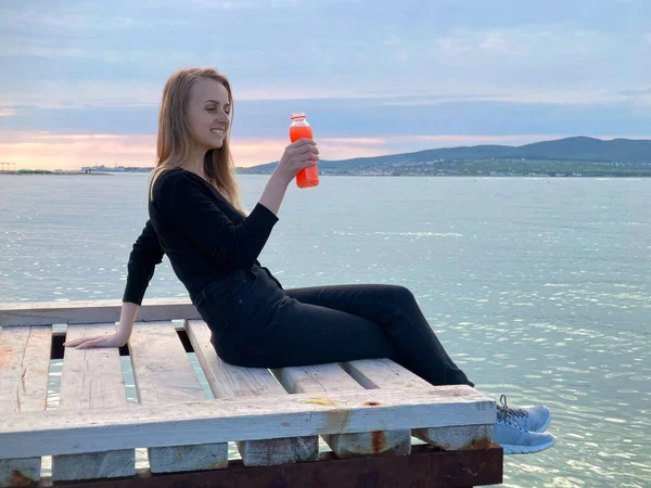 Donna che beve frullato di frutta dalla bottiglia sulla costa del mare — Foto Stock