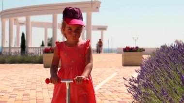 Little girl riding on scooter in summer park, slow motion