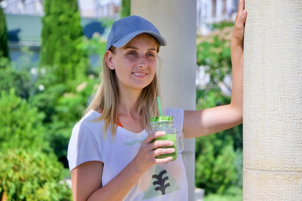 Mulher em tampa segurando vidro de smoothie verde e bebendo — Fotografia de Stock