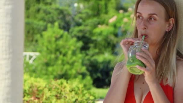 Блондинка в бікіні п'є зелену смужку на курорті — стокове відео