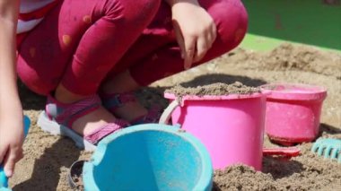 Küçük kız bahçede kum havuzunda oynuyor.