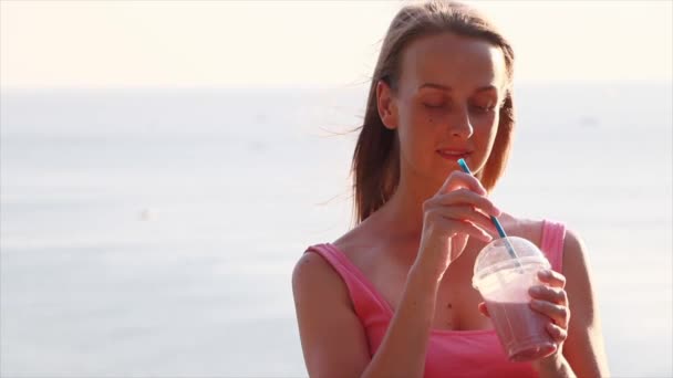Pembe elbiseli vejetaryen kadın deniz kenarında meyve suyu ile rahatlıyor. — Stok video