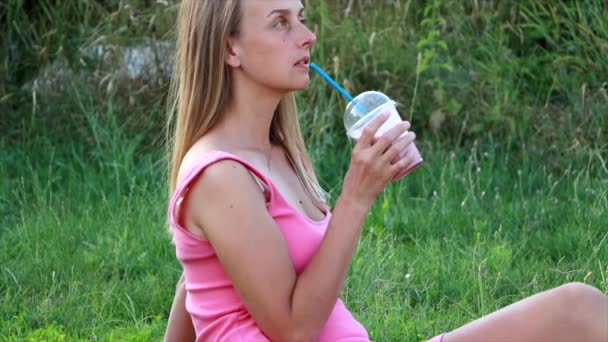 Femme végétalienne en robe rose se relaxe dans le parc avec smoothie aux baies — Video