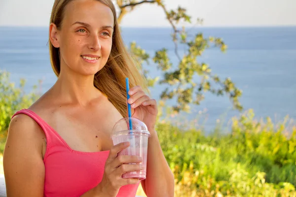 Vegan woman in pink dress is relaxing near sea cost with berry smoothie — Stock Photo, Image