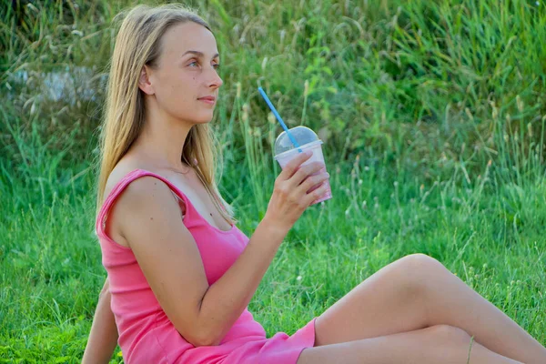 Vegan woman in pink dress is relaxing in the park with berry smoothie — Stock Photo, Image