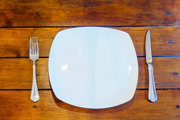 Plate and cutlery on wooden table top view. — Stock Photo, Image