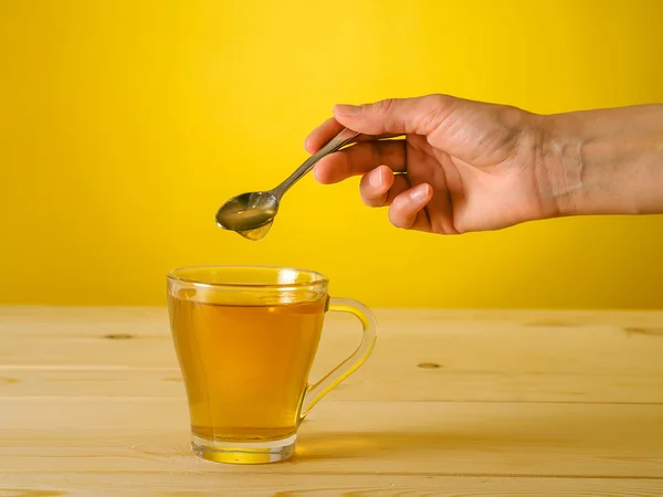 Honey falling from spoon in a glass of tea with lemon — Stock Photo, Image