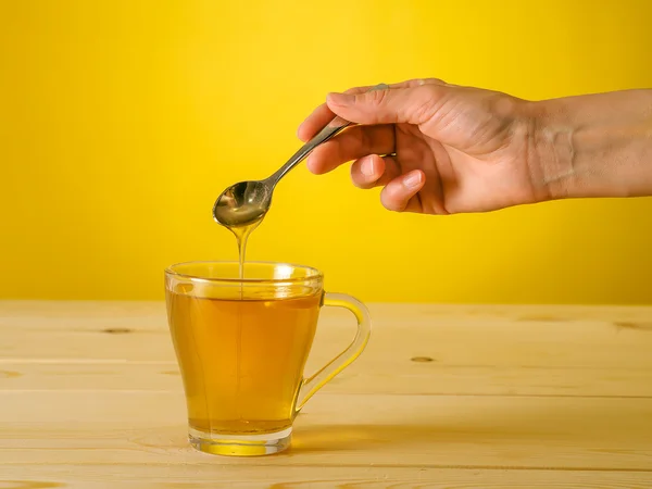 Honey falling from spoon in a glass of tea with lemon — Stock Photo, Image