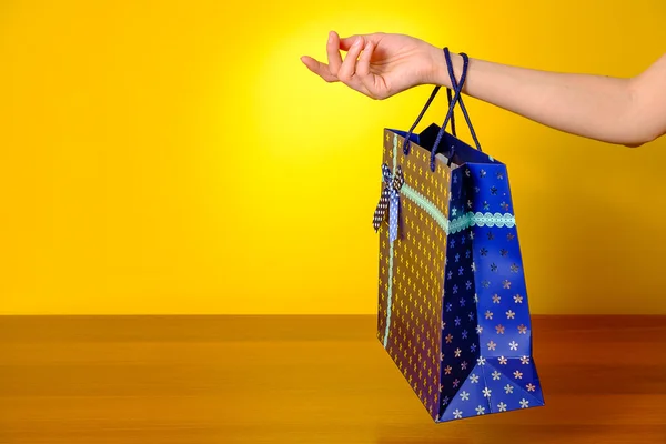 Mão feminina segurando saco azul no fundo amarelo — Fotografia de Stock