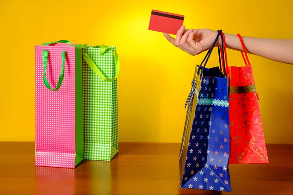 Ženská ruka drží nákupní tašky a kreditní kartu na žlutém podkladu — Stock fotografie