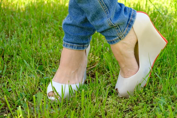 Piedi femminili in scarpe con zeppa tacchi su erba verde — Foto Stock