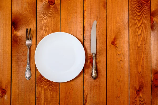 Piatto rotondo bianco vuoto con coltello antico e forchetta su fondo in legno. Vista dall'alto con spazio di testo . — Foto Stock