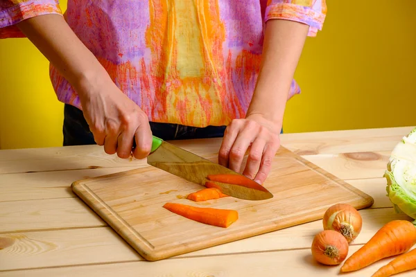 Mujer cortando zanahoria sobre tabla de madera y verduras a su alrededor — Foto de Stock