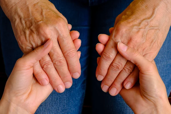 Руки молодой женщины, держащейся за руки пожилой женщины — стоковое фото
