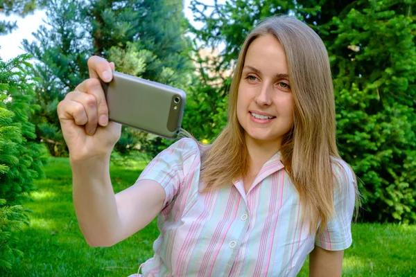 緑豊かな公園で屋外の selfie を作るのはかなり若い女性. — ストック写真